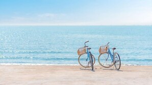 Dos bicicletas estacionadas en una playa arenosa con un mar azul y despejado al fondo.