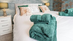Cama bem arrumada com roupa de cama verde e branca, toalha verde e almofadas decorativas.