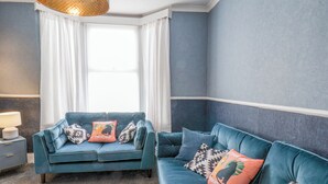 Um quarto com sofá azul, uma luminária e uma janela com cortinas.