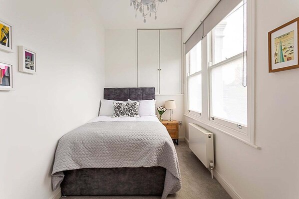 Un dormitorio con cama, mesita de noche, radiador y ventana.