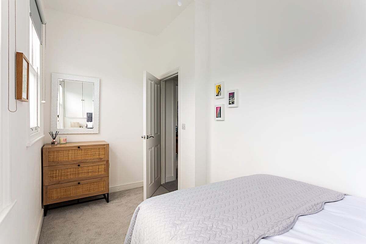A bedroom with a bed, a dresser, a mirror, and a door leading to another room.