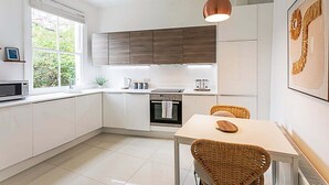 Una cocina moderna con armarios blancos, horno empotrado, microondas y un comedor con mesa y sillas de mimbre.
