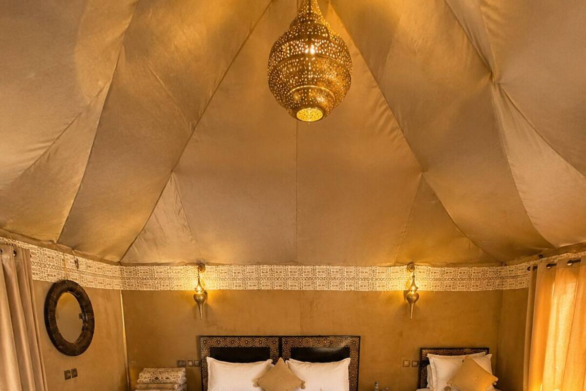 A tented room with a large bed, two smaller beds, a patterned rug, and a hanging light fixture.