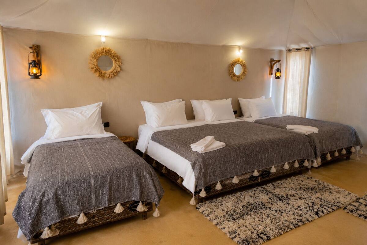 A hotel room with three beds, a patterned rug, and wall-mounted lanterns.