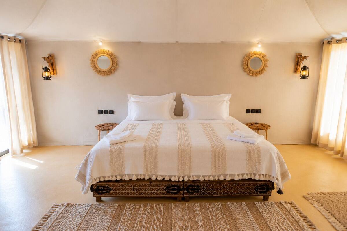 A spacious bedroom with a large bed, two nightstands, a wooden headboard, and decorative wall sconces.