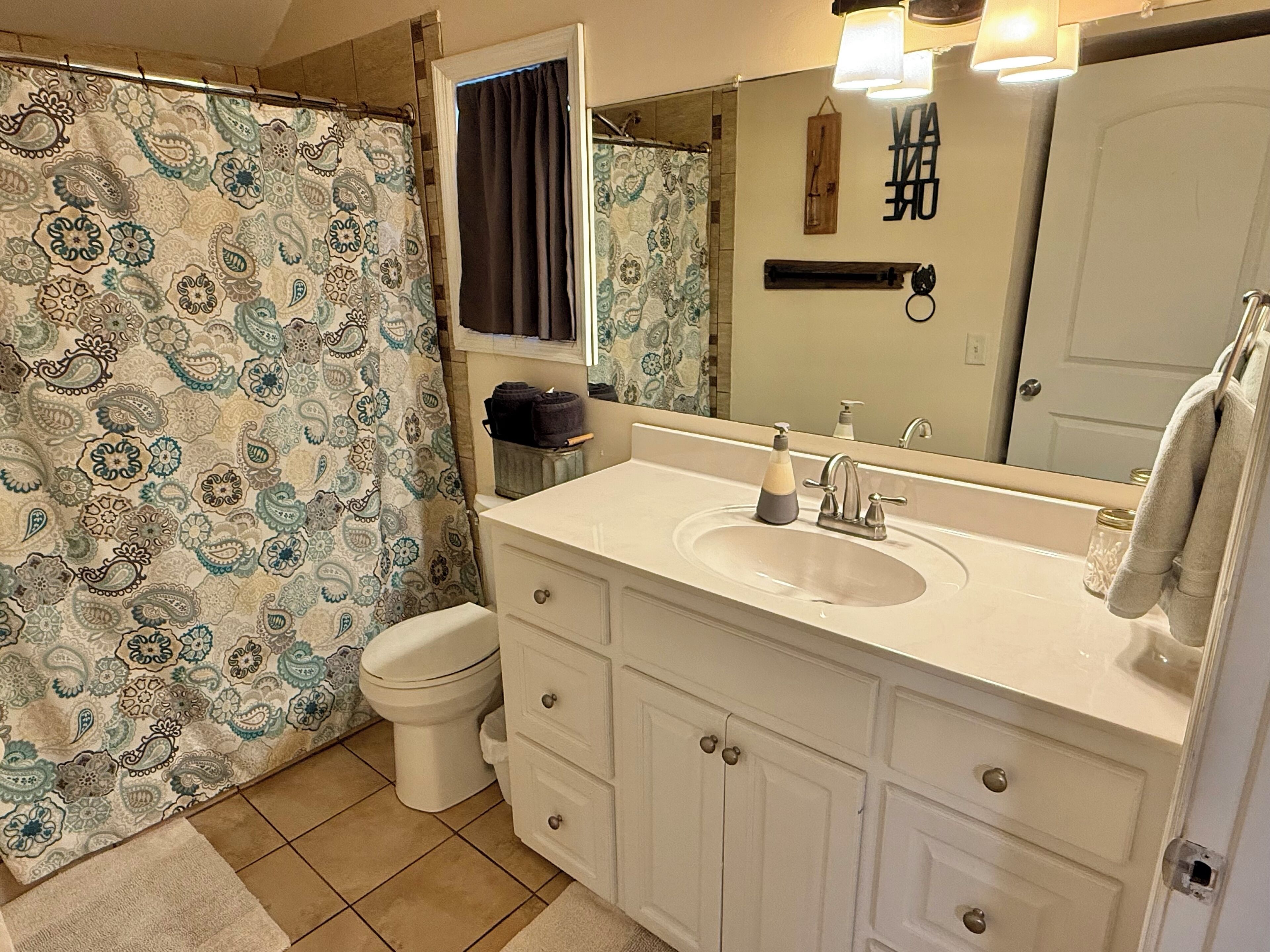 Un baño con cortina de ducha estampada, inodoro, lavamanos con espejo y barra para toallas.