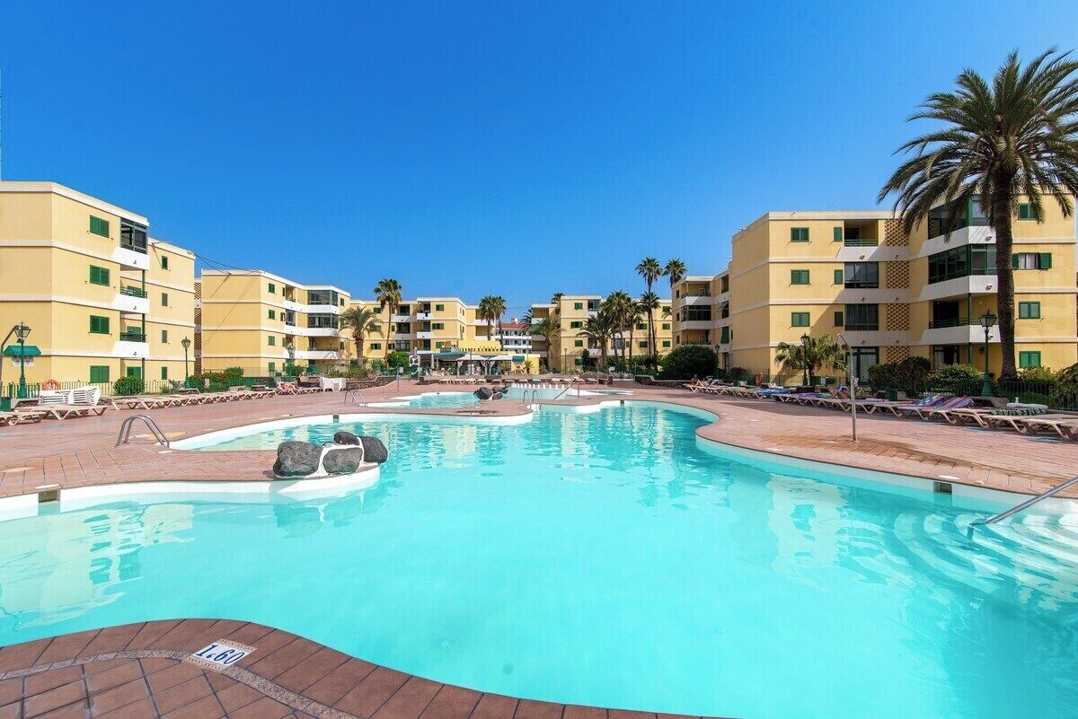 Una piscina di un resort con acqua cristallina, circondata da edifici gialli e palme.