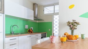 Cocina moderna con baldosas verdes, armarios blancos y una mesa de madera con alimentos para el desayuno.
