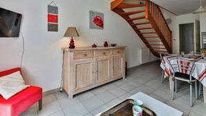 Una sala de estar con un sofá rojo, un aparador de madera, una mesa de comedor con sillas y una escalera.