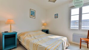 Un dormitorio con una cama, dos mesitas de noche, una silla, un ventanal y un radiador.