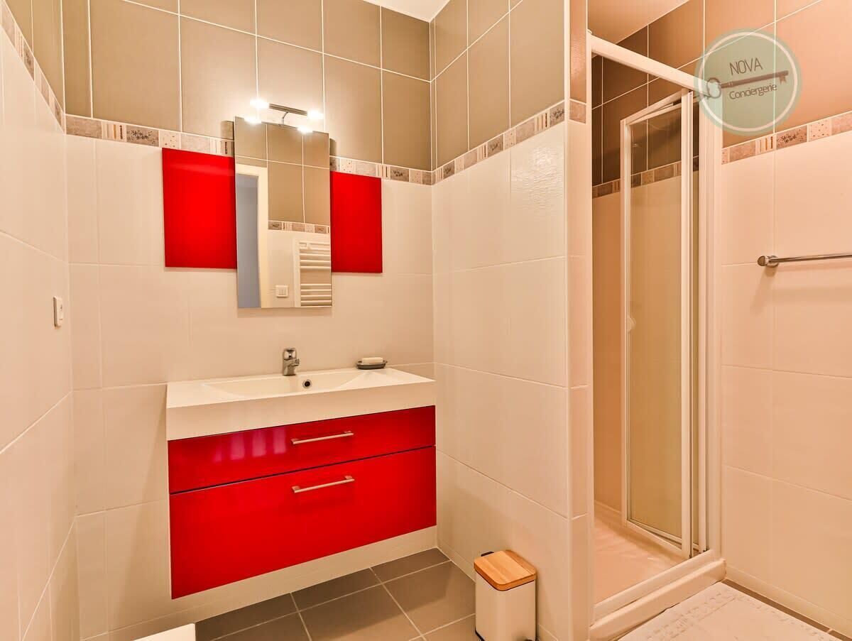 Ein Badezimmer mit einem weißen Waschbecken, einem roten Schrank und einer Duschkabine aus Glas.