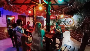 A restaurant with wooden tables and chairs, a thatched roof, and string lights. - EL CURICHAL HOSTEL (Rurrenabaque)