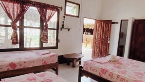 A room with two beds, a ceiling fan, wooden beams, a window with curtains, a small table, and a door leading to another room. - EL CURICHAL HOSTEL (Rurrenabaque)