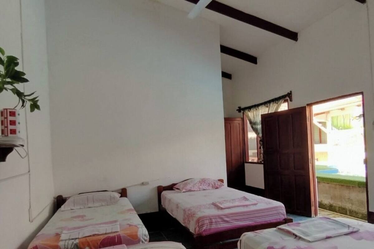 A room with three beds, a ceiling fan, and a door leading to an outdoor area.