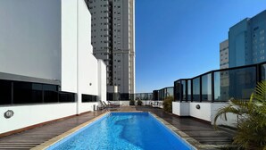 A rooftop pool with wooden decking, surrounded by white walls and large windows. - PRIME LOK- SP FLAT JARDINS II (São Paulo)