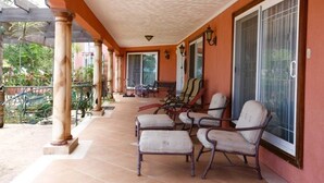A covered porch with a tiled floor, columns, and a row of cushioned chairs. - Villa Paradise- Pool, Jacuzzi & More (Montego Bay)