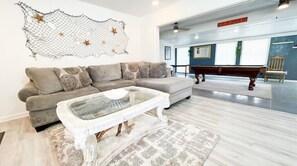 Relax in a spacious living area with a large sectional sofa and coffee table, complemented by a decorative rug and billiards table.