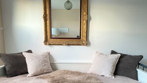 Ein Schlafzimmer mit einem Bett, zwei Kissen, einem flauschigen Teppich und einem Spiegel mit goldener Rahmung.