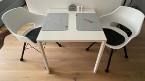 Ein kleiner, weißer Tisch mit zwei grauen Unterlayser und zwei weiße Stühle mit schwarzen Kissen.
