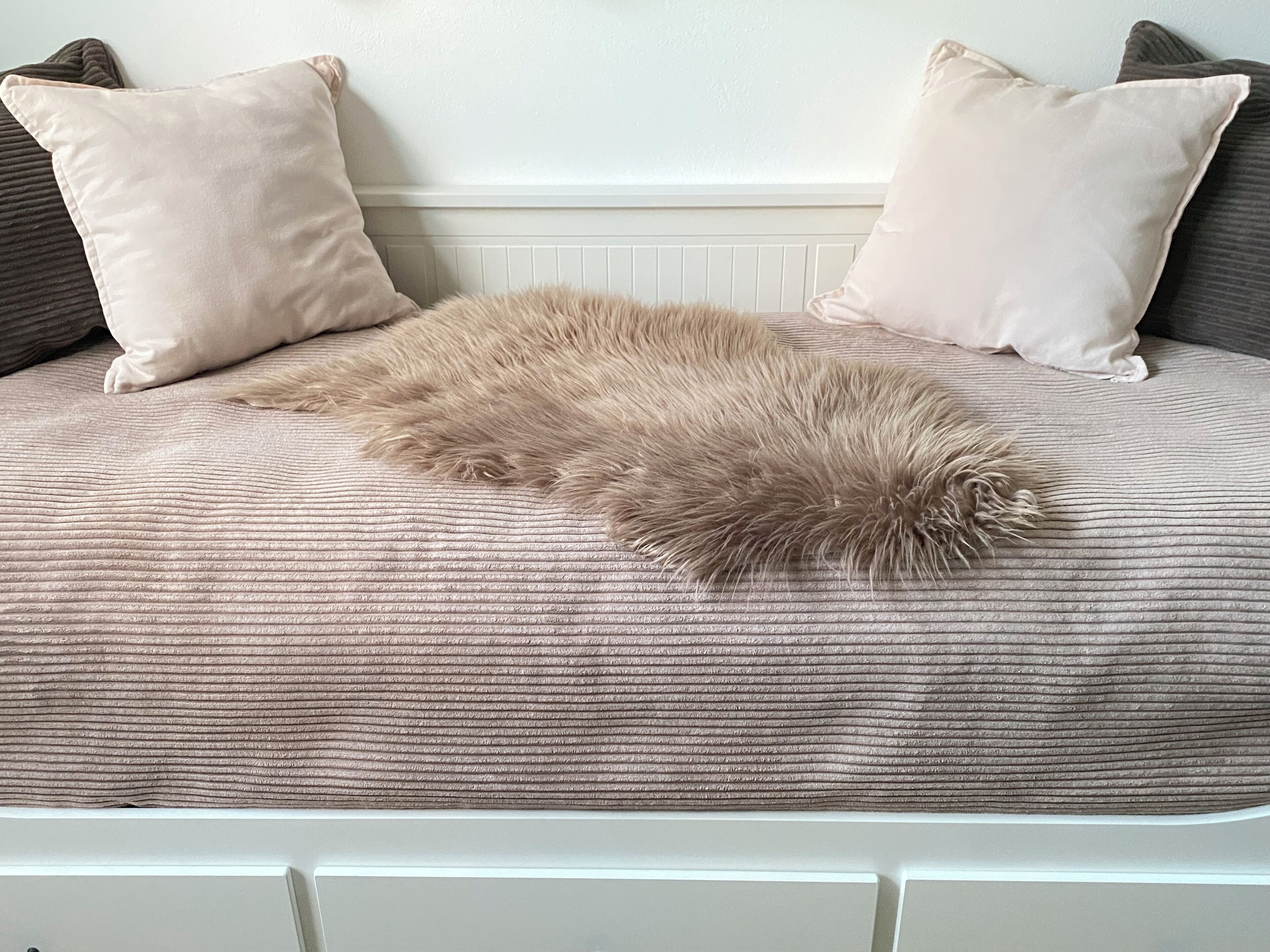 Ein Bett mit einer beige farbenen Decke und zwei Kissen, eines dunkel, eines hell.