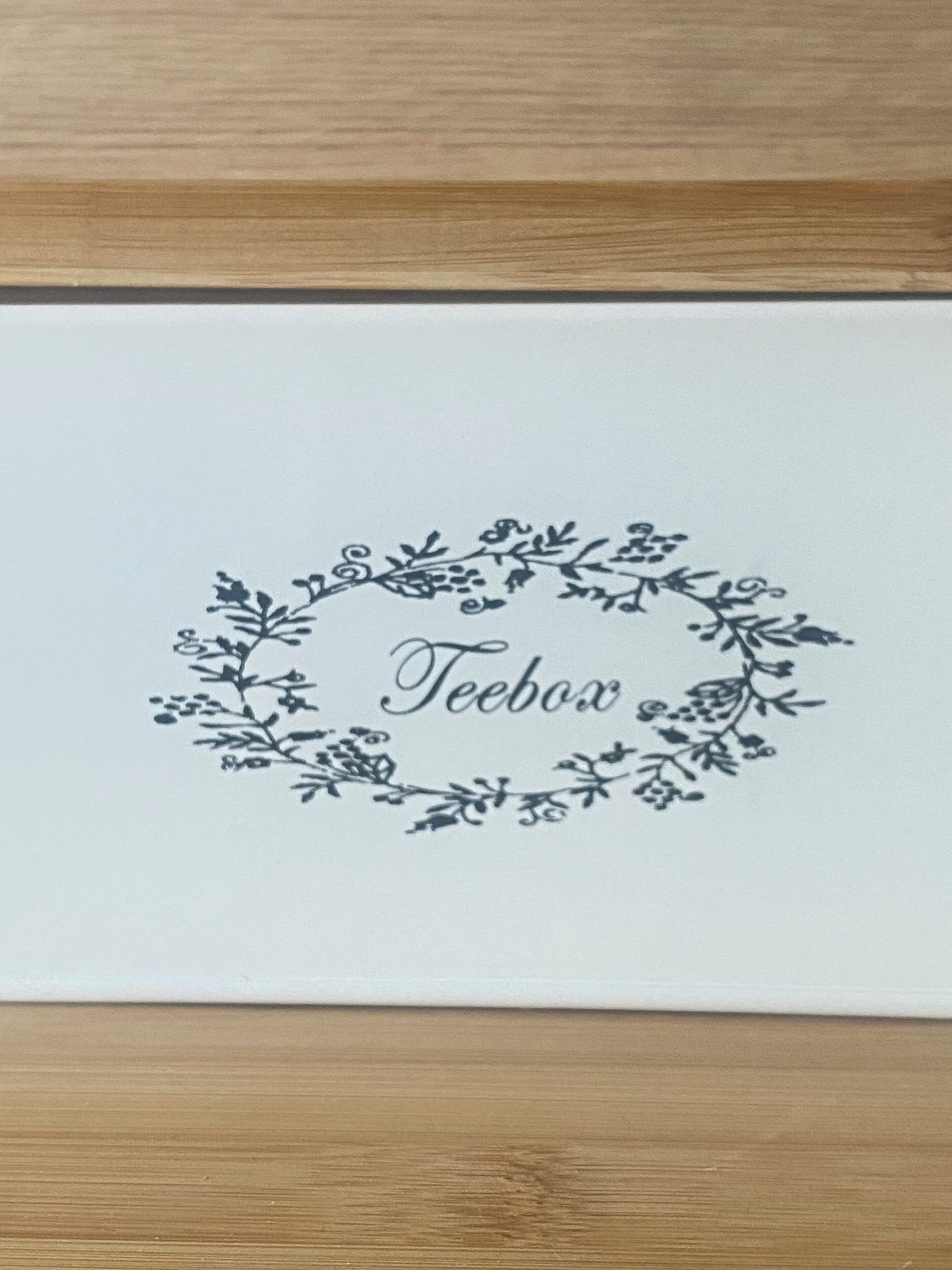 Une carte blanche ornée d’un motif floral, avec le mot « Teebox » inscrit au centre.