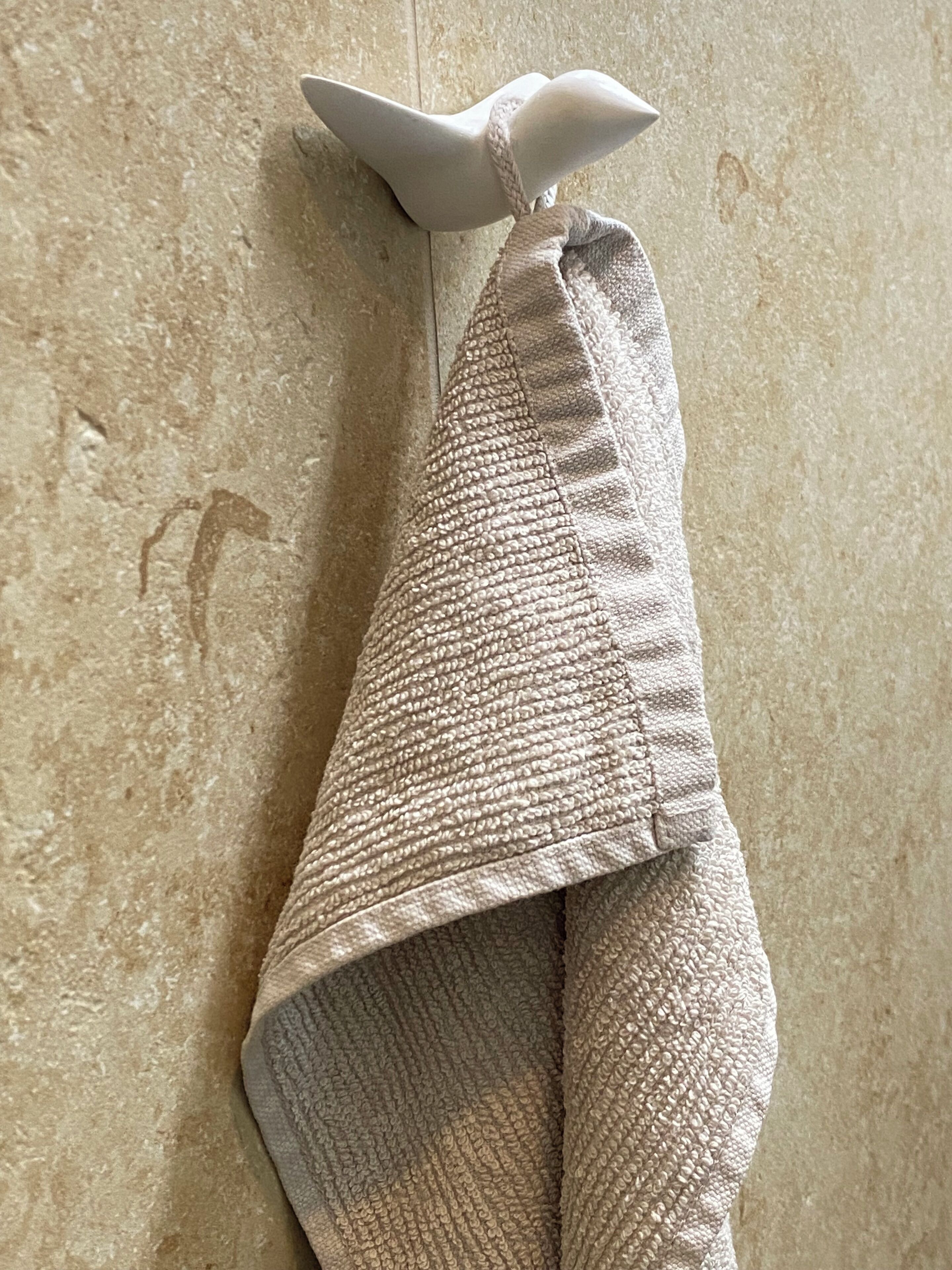 Et beige håndklæde med struktur hænger på væggen.