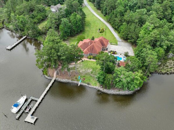 An aerial view of a house surrounded by dense greenery and a body of water.