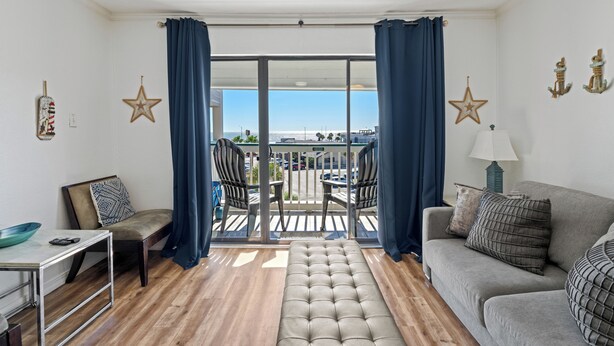 A living room with a sofa, a bench, a table, and a balcony with chairs. - Beach Front TOP FLOOR! Ocean Views!POOL (Galveston)