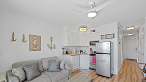 A modern kitchen with white cabinetry, a stainless steel refrigerator, and a wooden floor. - Beach Front TOP FLOOR! Ocean Views!POOL (Galveston)