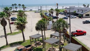 A parking lot with a view of the beach and ocean, surrounded by palm trees and a few buildings. - Beach Front TOP FLOOR! Ocean Views!POOL (Galveston)