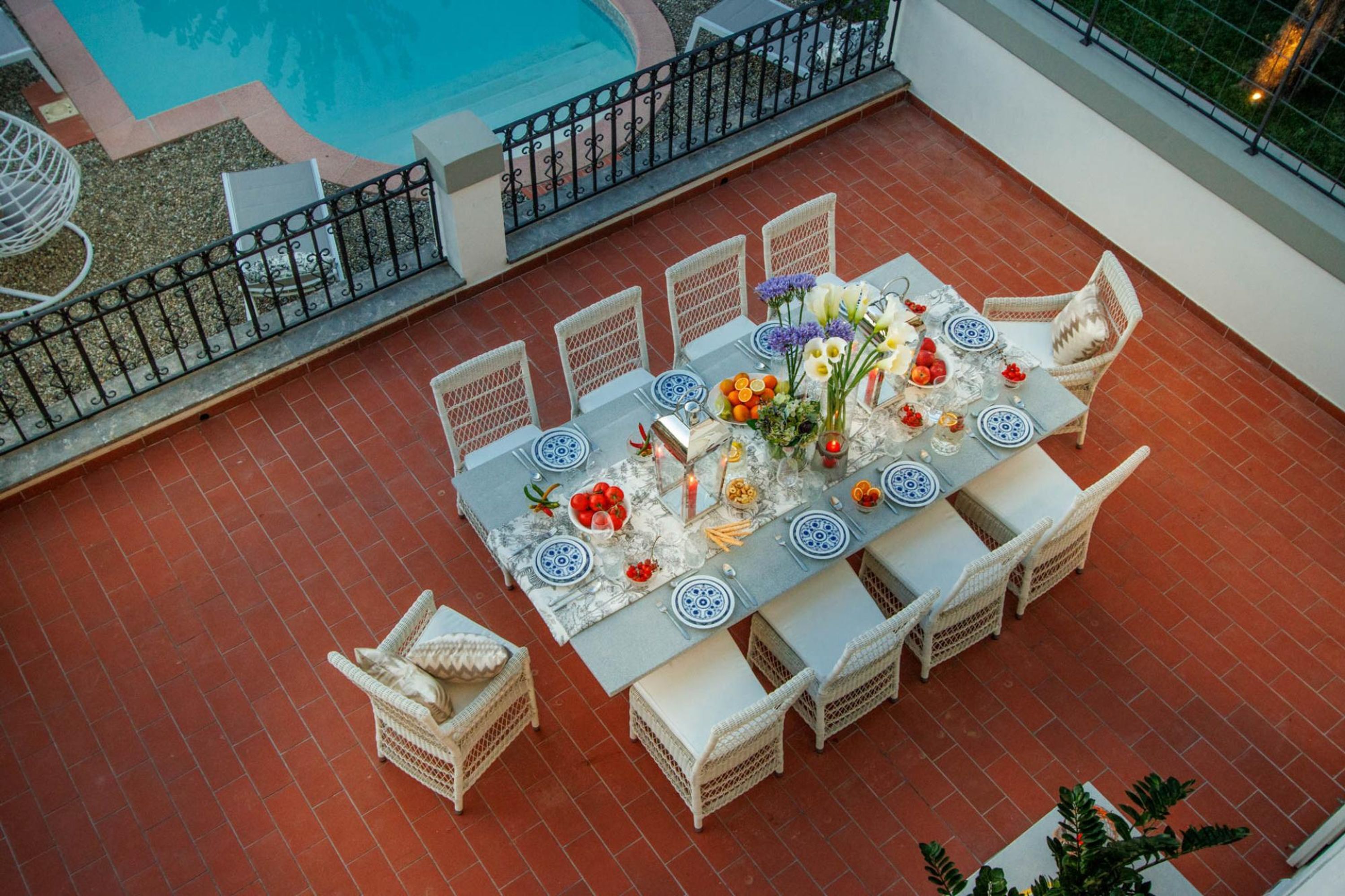 A dining area with a pool view, white wicker chairs, and a table set with blue and white plates and flowers.