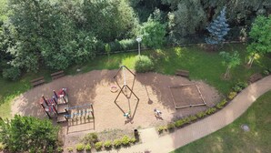 Vista aérea de un parque con un área de juegos infantiles, una zona para jugar en tierra y un camino pavimentado.