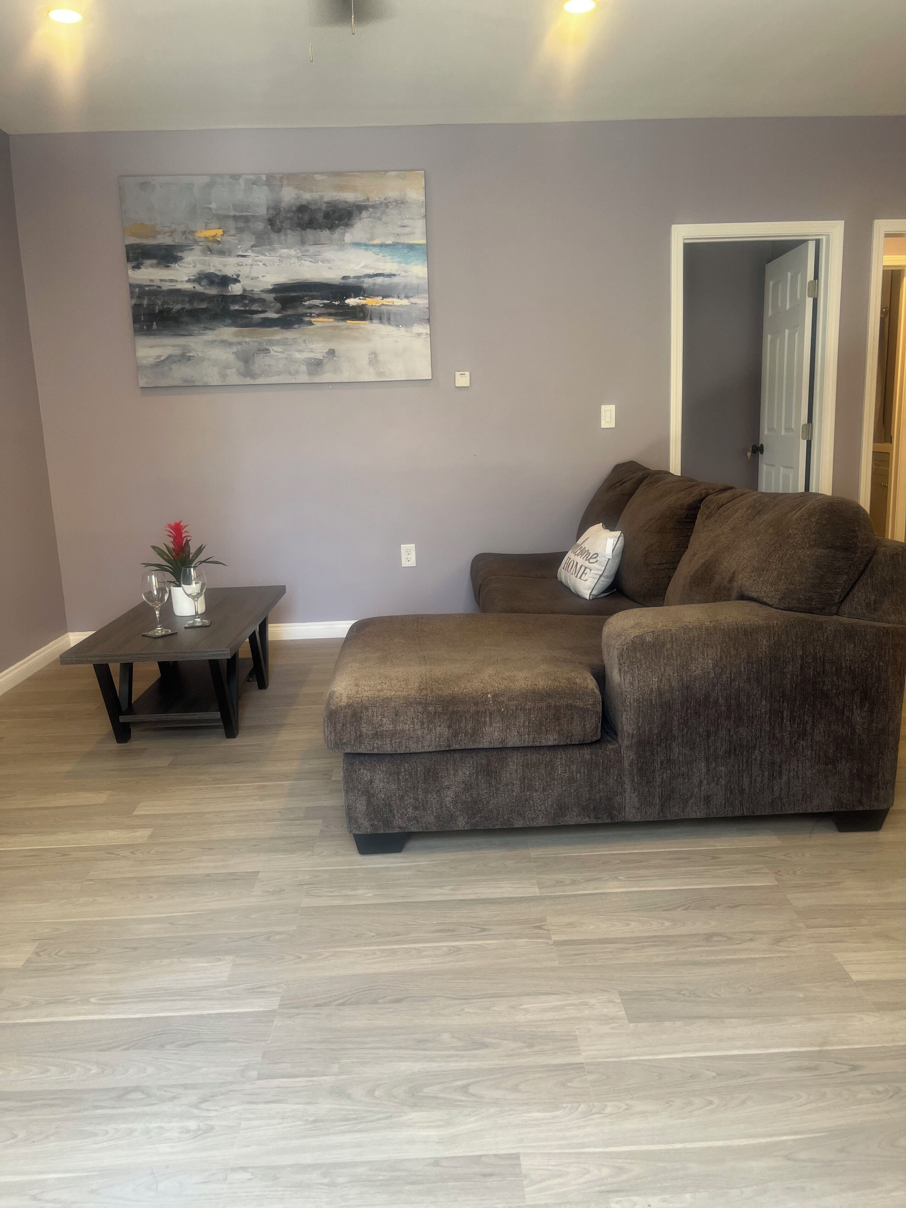 Uma sala de estar com sofá seccional, mesa de centro e um quadro na parede.