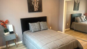 A bedroom with a large bed, a nightstand, a mirror, and a painting on the wall. - Guest House in the beautiful City of Downey (Downey)