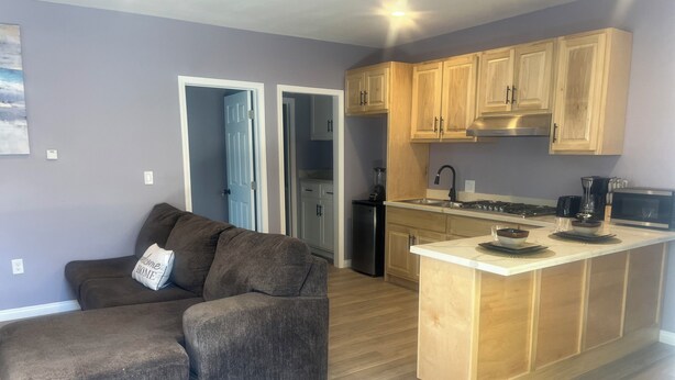 A modern kitchen with wooden cabinets, a central island, and a built-in stove. - Guest House in the beautiful City of Downey (Downey)