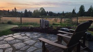 A patio with stone flooring and wooden chairs, overlooking a pond and trees. - The Nest!! (Lantzville)