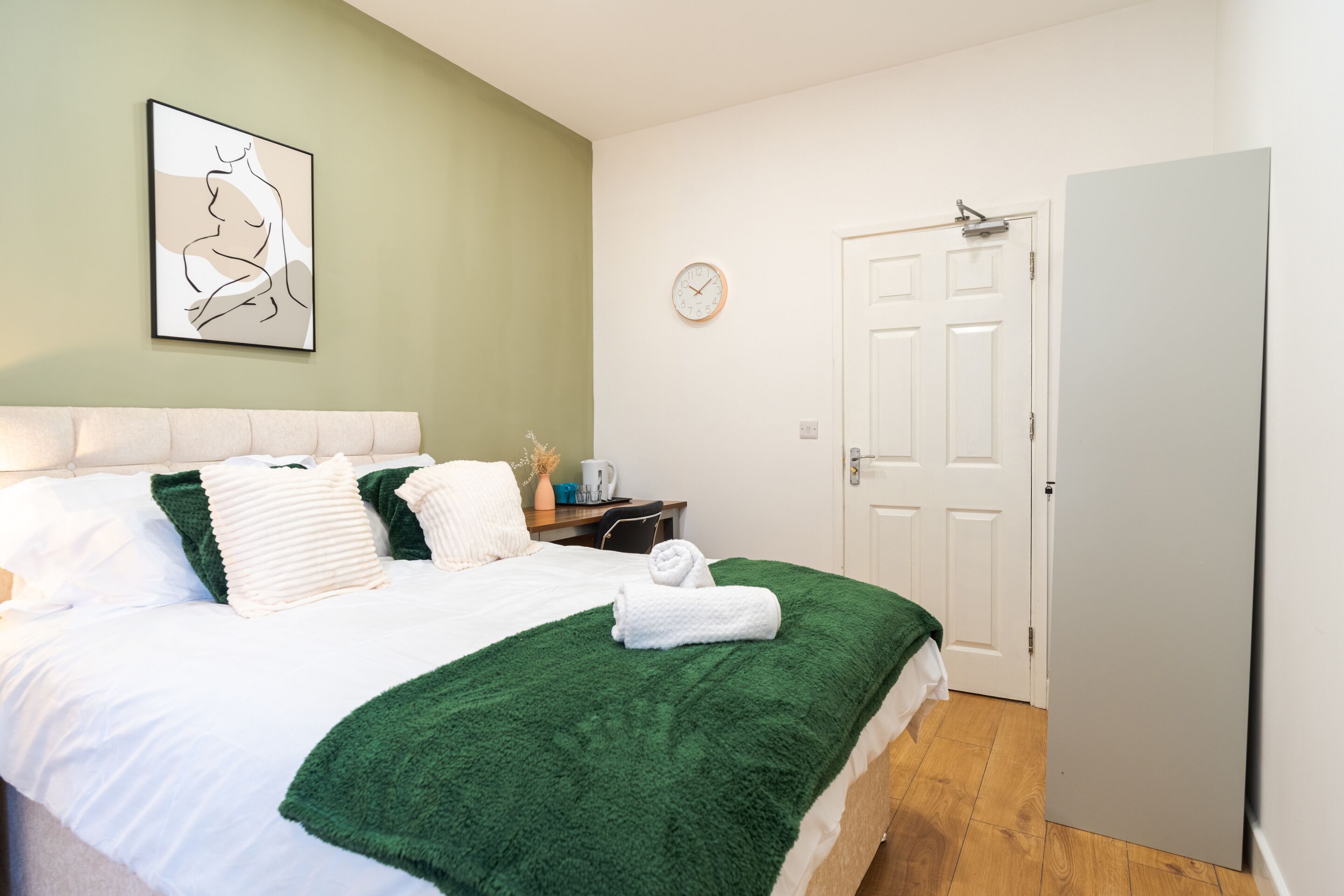 A neatly arranged bedroom with a bed, a bedside table, a clock, and a door.
