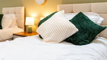 Una cama bien hecha con almohadas blancas y verdes, una lámpara de noche y un reloj en la pared.