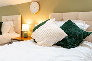 Una cama bien hecha con almohadas blancas y verdes, una lámpara de noche y un reloj en la pared.