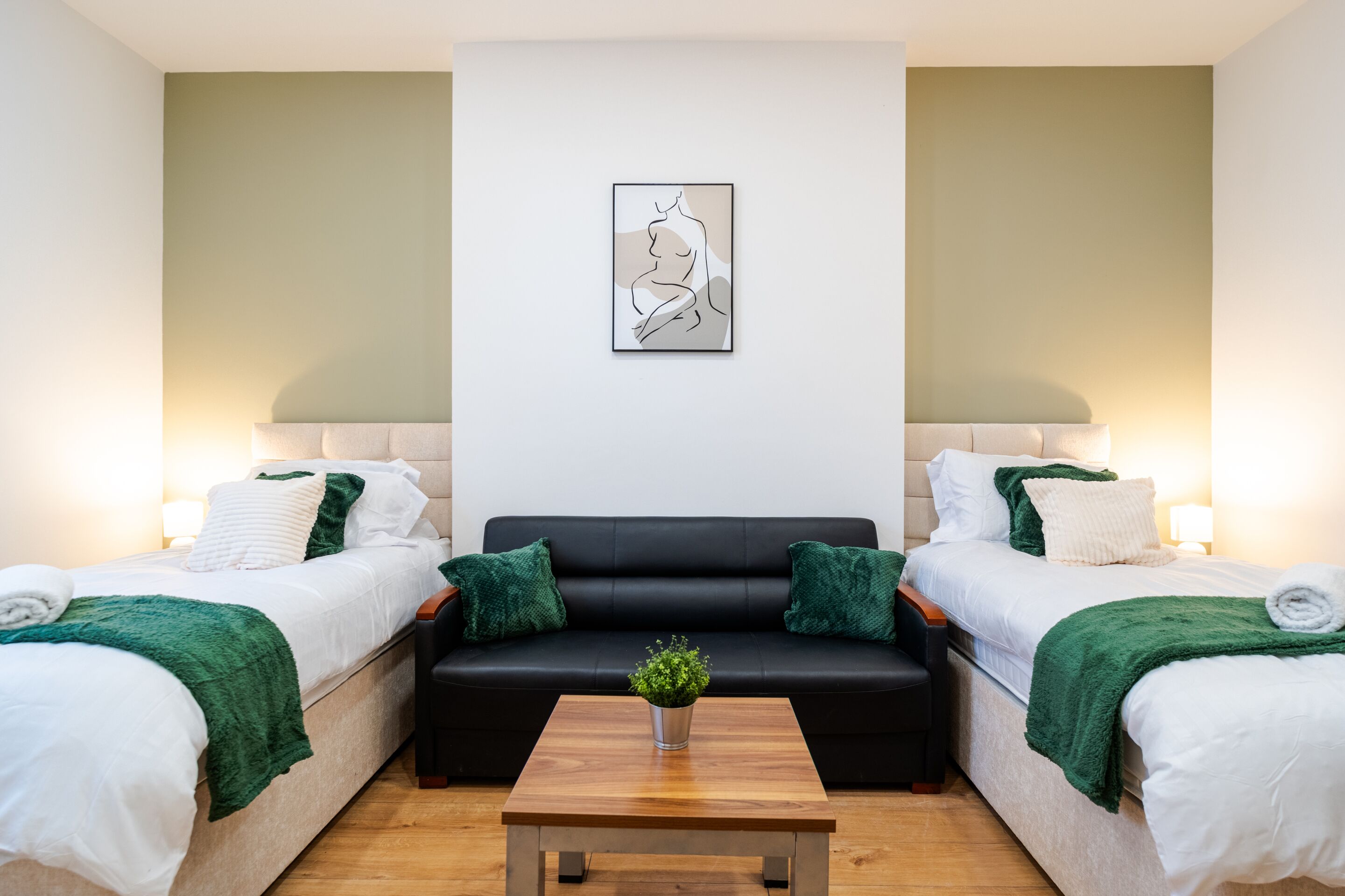 A room with two beds, a sofa, a coffee table, and a wall-mounted artwork.
