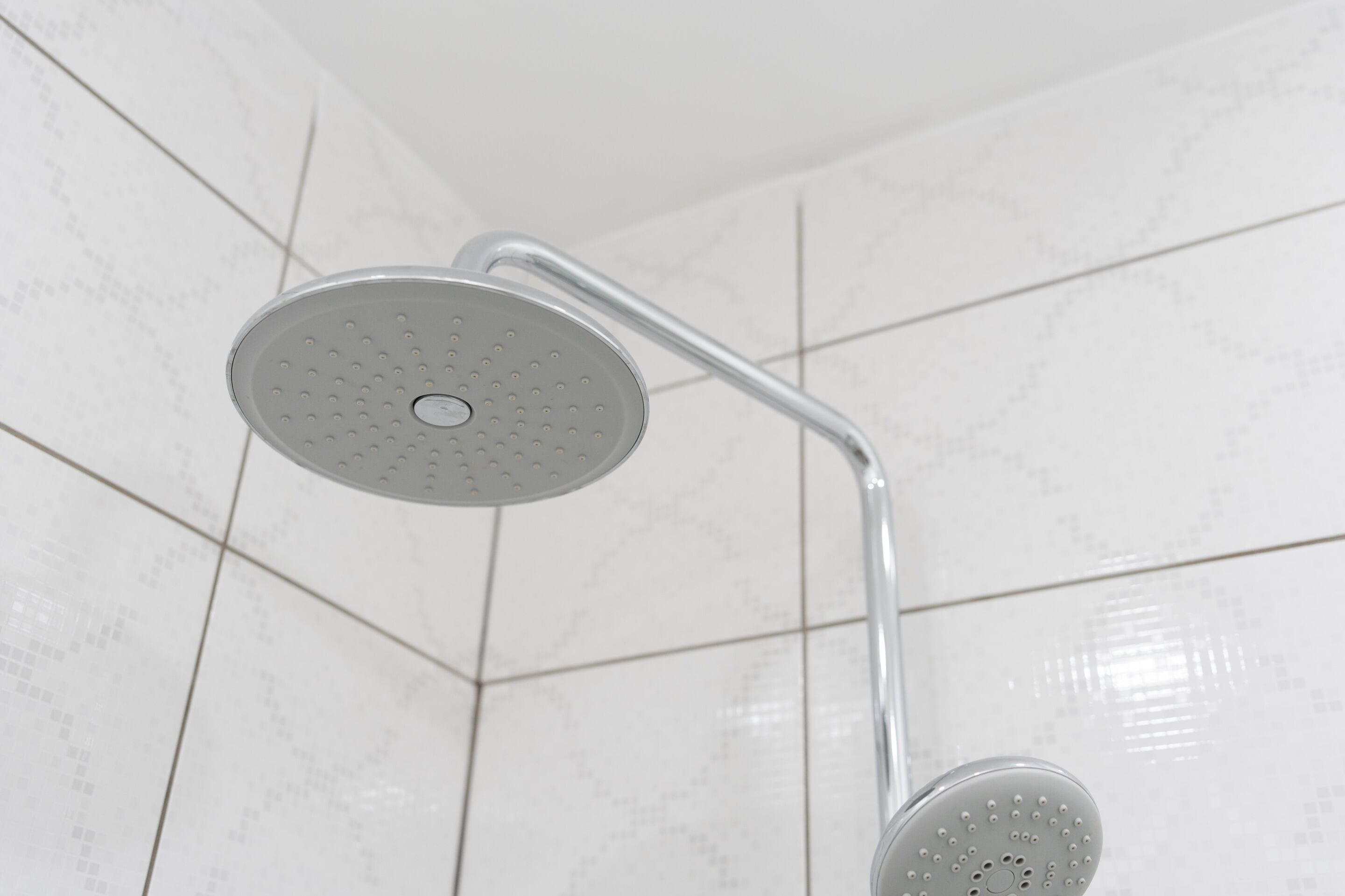 Ducha con cabezal redondo y grifo de mango curvo, frente a una pared de azulejos.