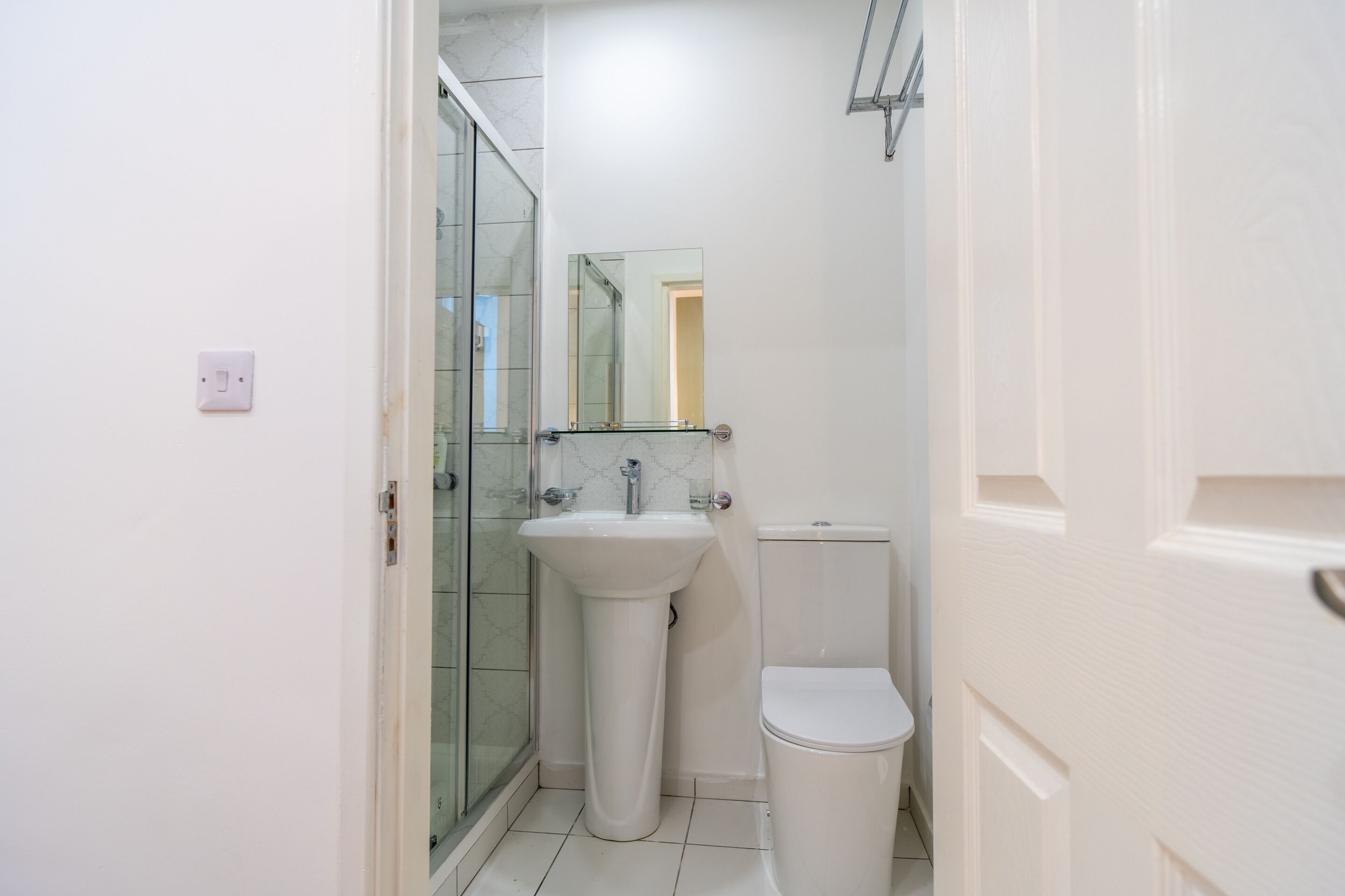 A small, white bathroom with a glass shower enclosure, a pedestal sink, and a toilet.