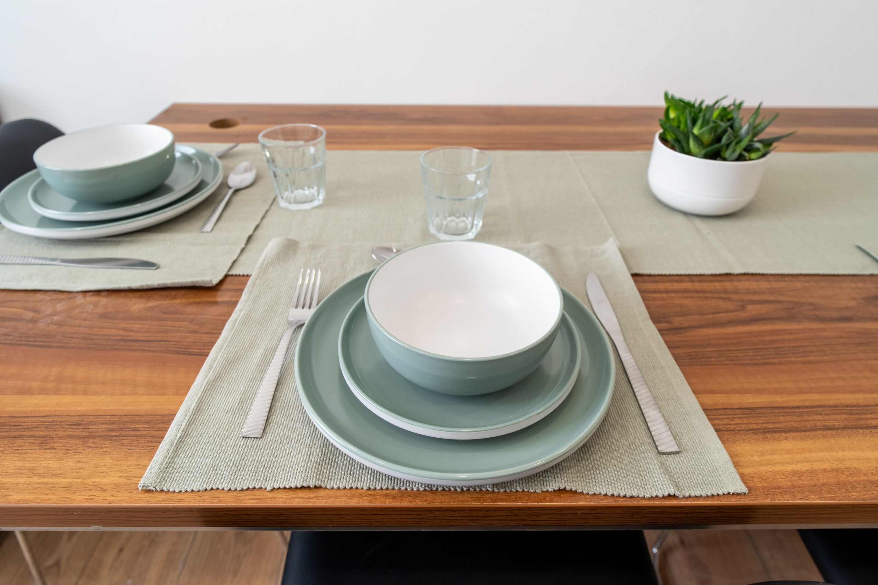 A dining table set with plates, bowls, cutlery, glasses, and a potted plant.