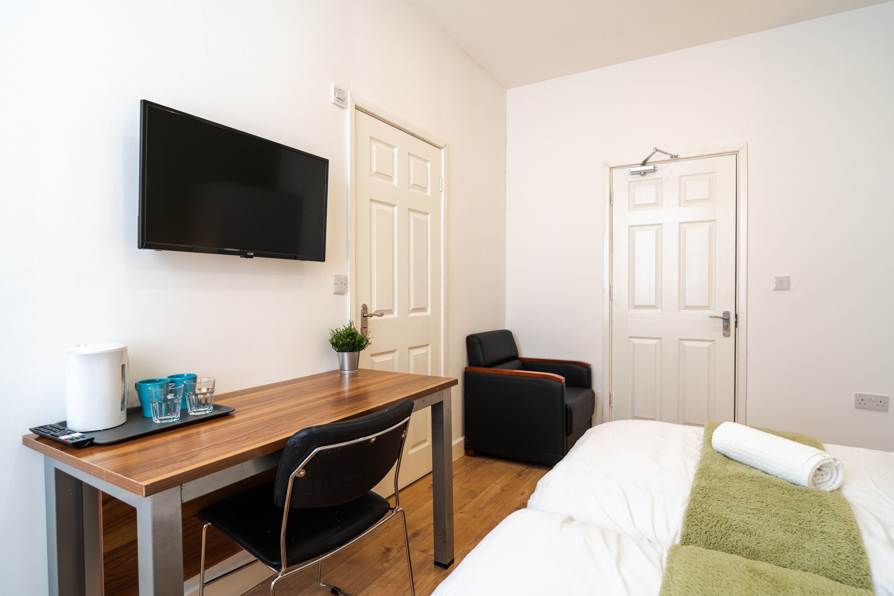 A hotel room with a bed, a desk with a chair, a television, and two doors.