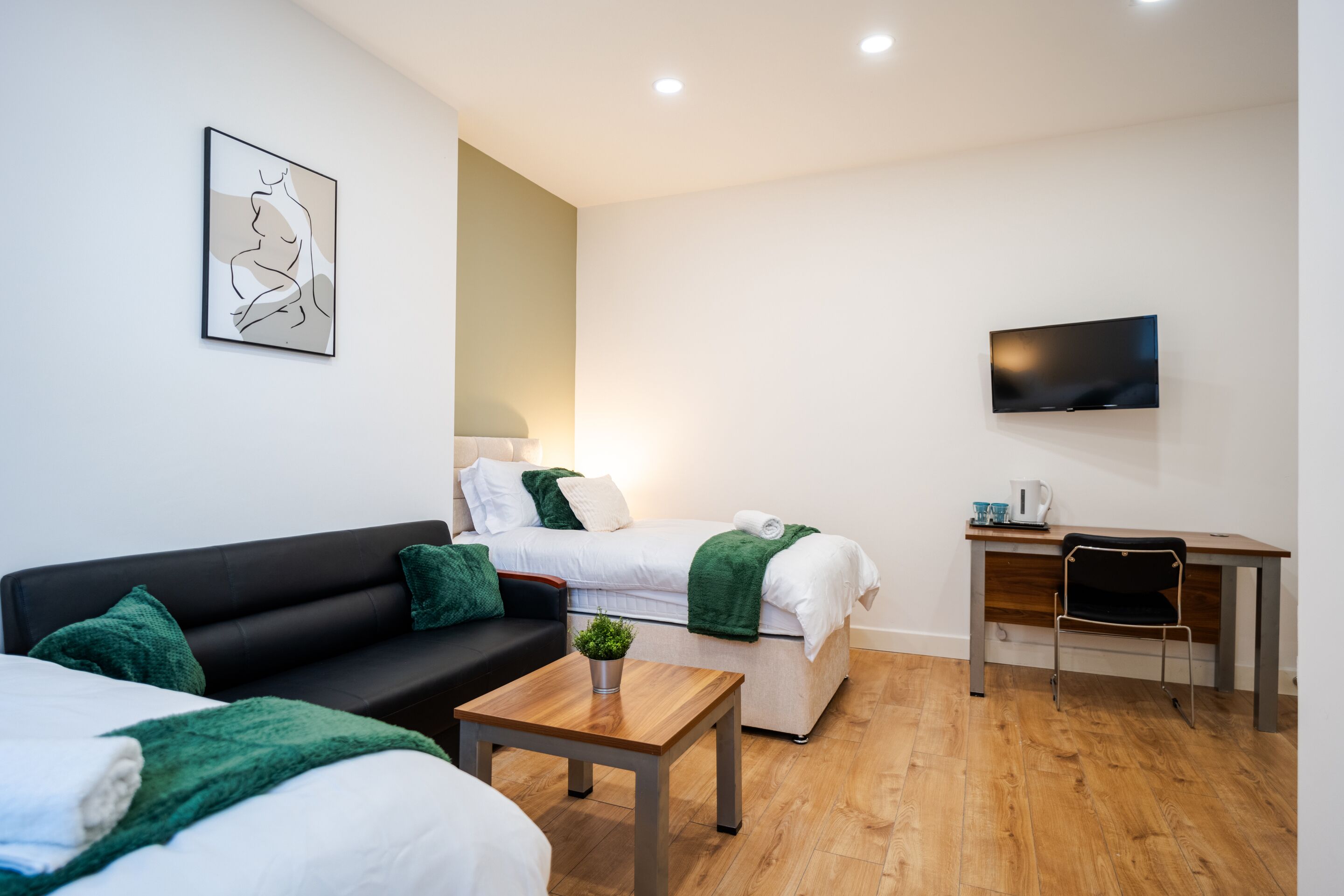 A modern hotel room with a sofa, two single beds, a desk, a TV, and a small table with a plant.