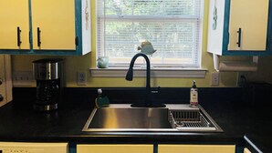 Een keuken met een roestvrijstalen spoelbak, een koffiezetapparaat en een raam met jaloezieën.
