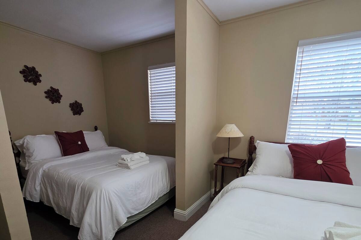 A hotel room with two beds, a nightstand, a lamp, and a window with blinds.
