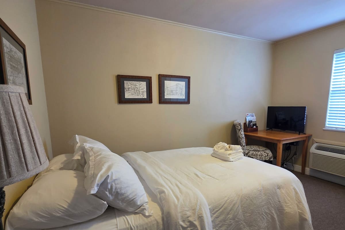 A neatly made bed with white linens, a television on a wooden stand, and two framed pictures on the wall.