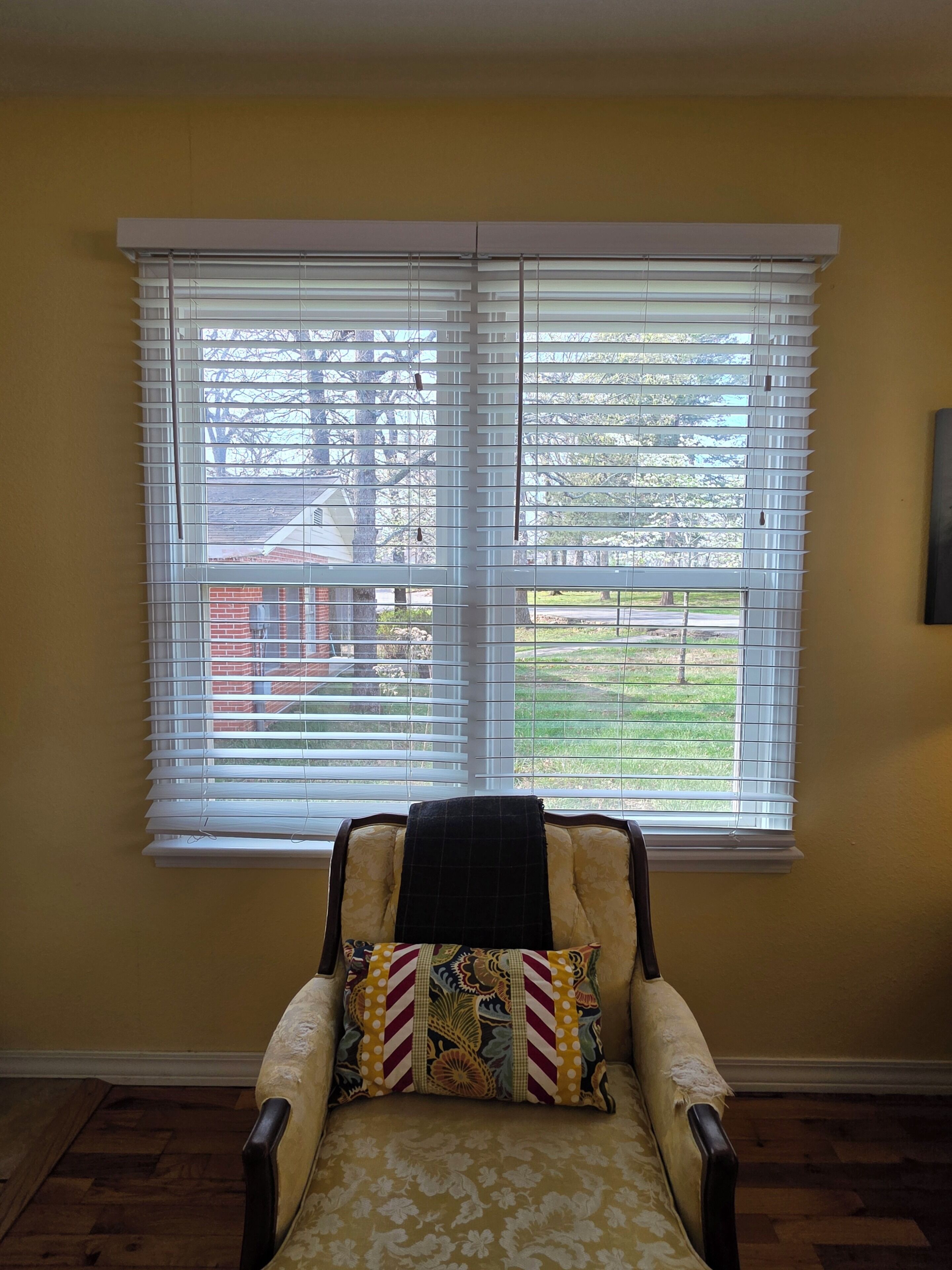 Una habitación con una ventana, una silla con un cojín estampado y un cuadro en la pared.