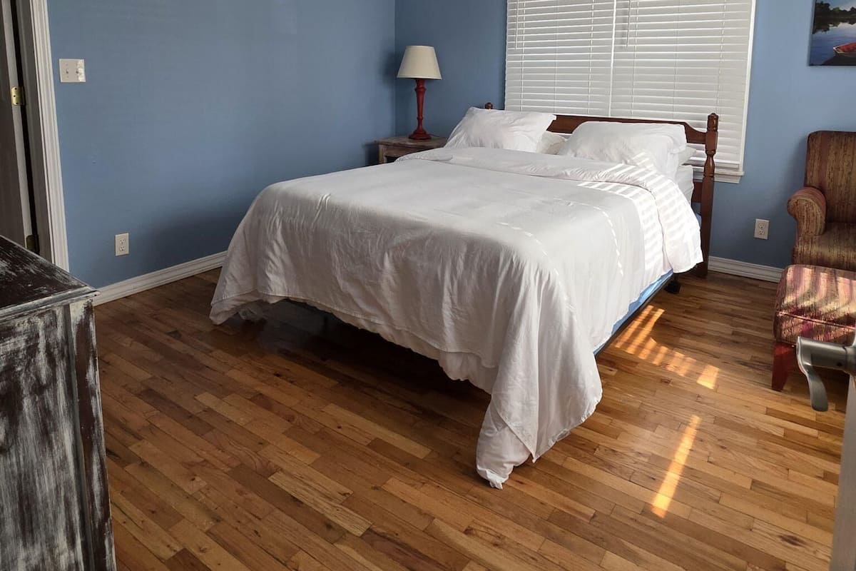 A bedroom with a bed, a ceiling fan, a window with blinds, a lamp, and a chair.